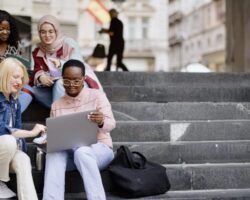 Students sit on the steps near the college and look at the laptop and digital tablet and talk